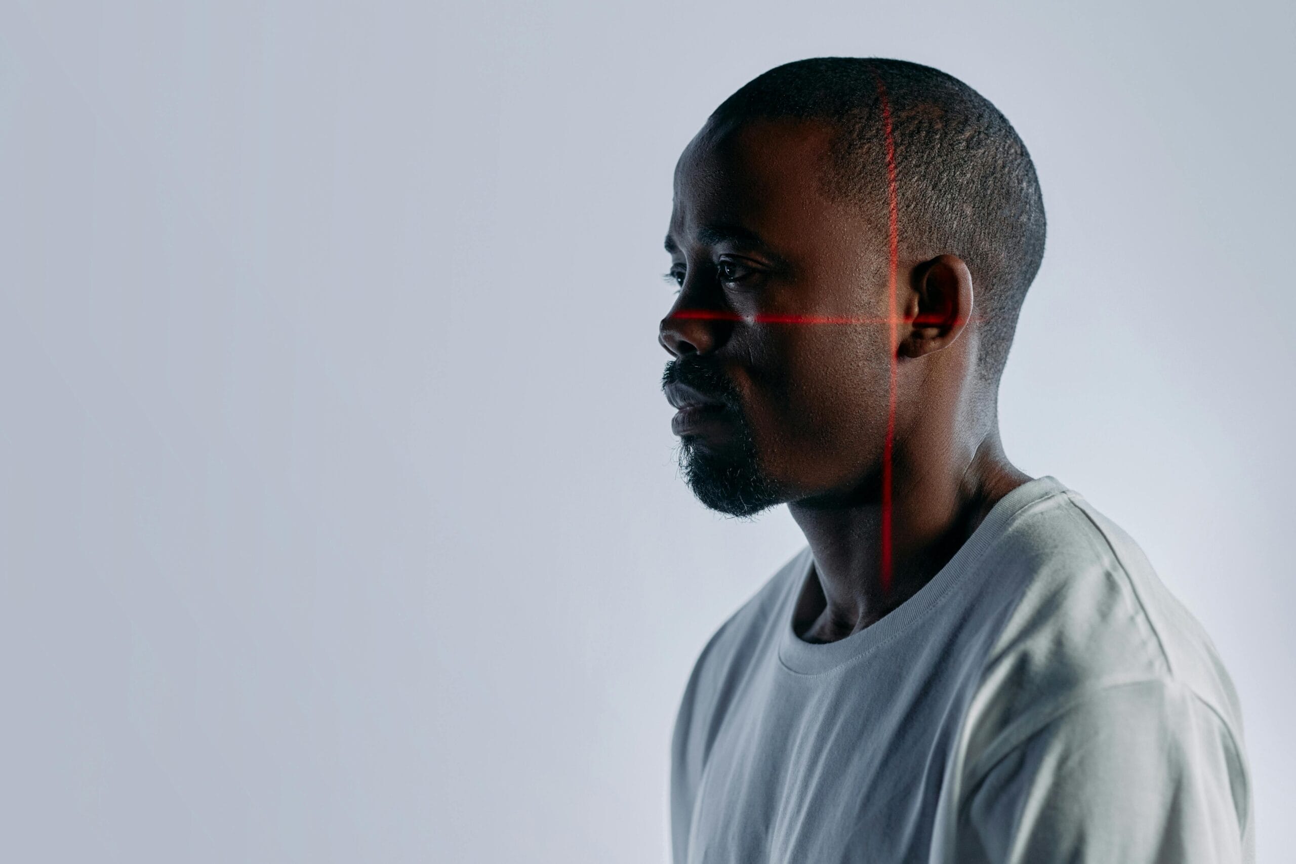 A man in a white t-shirt undergoing a 3D facial scan with red laser lines in a studio.